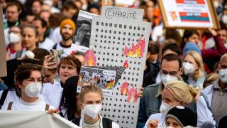 Archivbild: Ärzte stehen am 05.10.2022 bei einem Warnstreik an der Charité mit einem Schild mit einem brennenden Bettenhaus. (Quelle: dpa/Fabian Sommer)